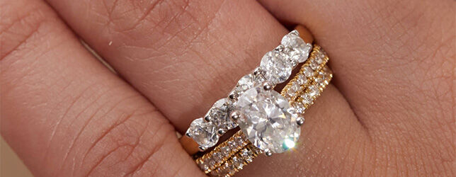 Oval cut diamond engagement ring stacked with gold pavé bands and five-stone diamond ring